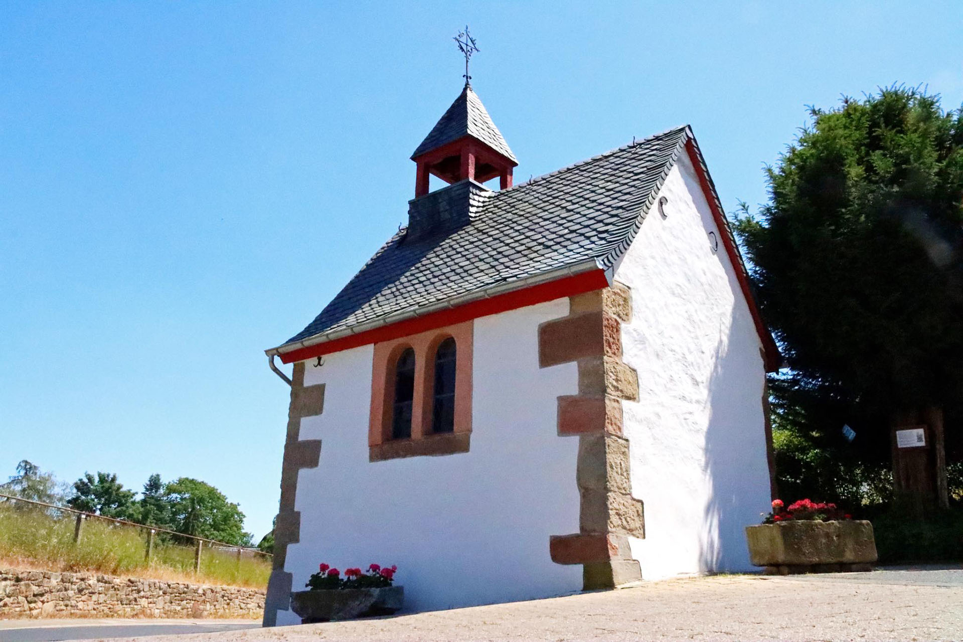 Das Bild zeigt eine weiße Kapelle in Berzbuir am unteren Ende eines Berges. 